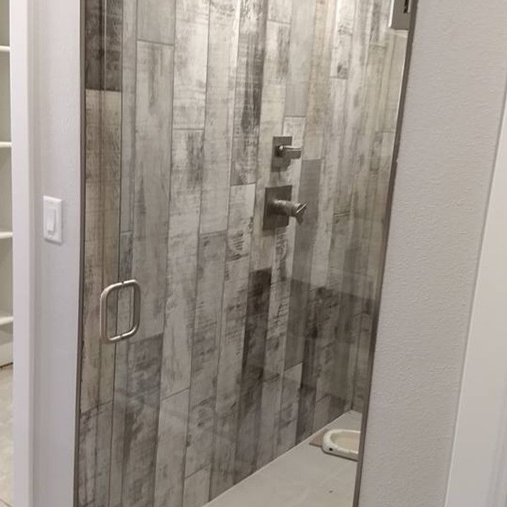 Shower with gray, wood-look tile walls, glass door, and silver hardware. A light switch is on the left.