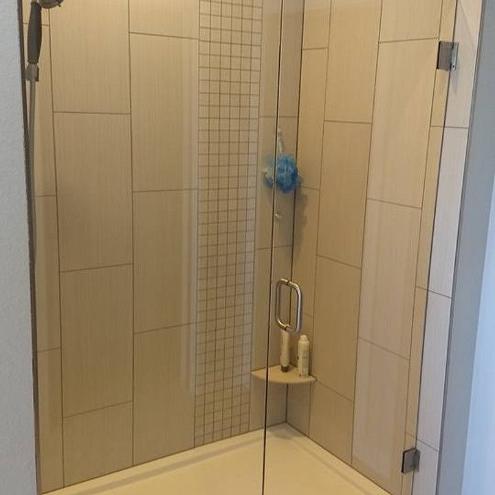 Glass shower enclosure with beige tiled walls, a small shelf, and a hanging blue sponge.
