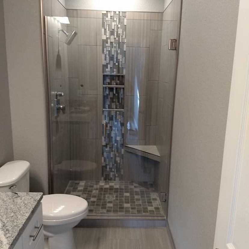 Modern bathroom with glass-enclosed shower, gray tile, mosaic accent, and a built-in bench.