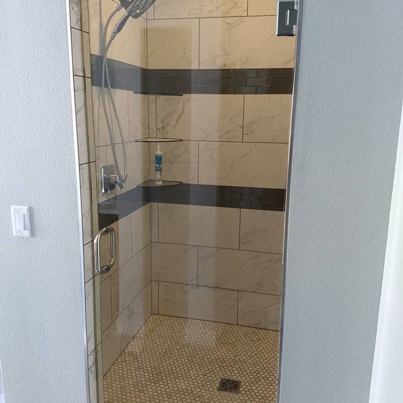 Glass-door shower with white and dark gray tiled walls and a small mosaic tile floor.
