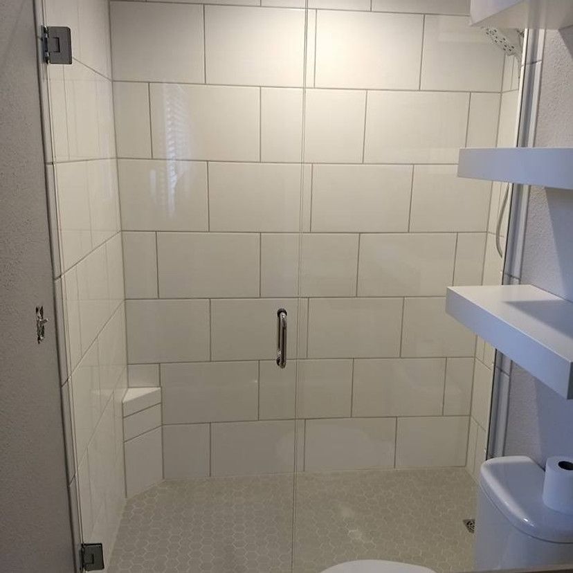 White-tiled shower with glass door and built-in bench. Two shelves are mounted on the right.