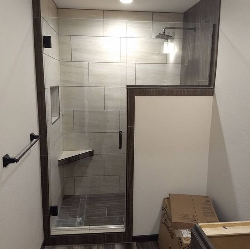 Shower with tile walls, glass door and panel, dark trim, and a towel bar.