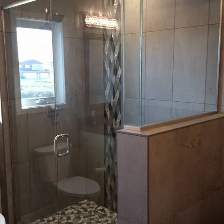 Bathroom with glass shower door, toilet, and window, neutral-toned tiles, decorative strip on shower wall.
