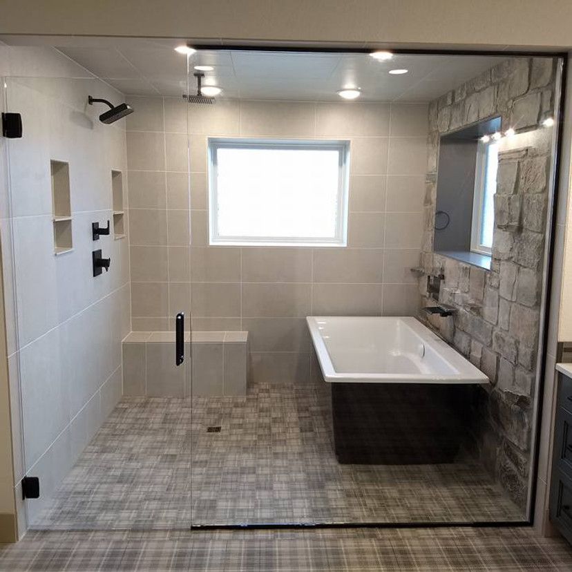 Modern bathroom with glass shower, stone accent wall, and soaking tub.