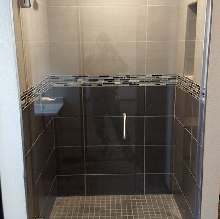 Gray-tiled shower with a glass door, mosaic border, and a dark-tiled back wall.