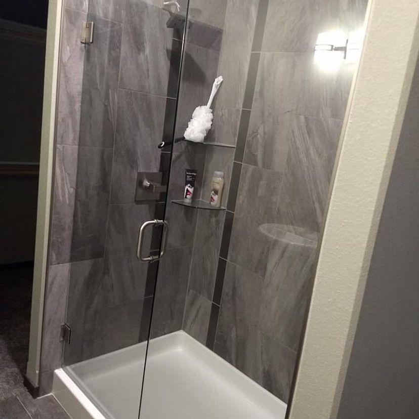 Gray tiled shower with glass door and shelf holding toiletries.