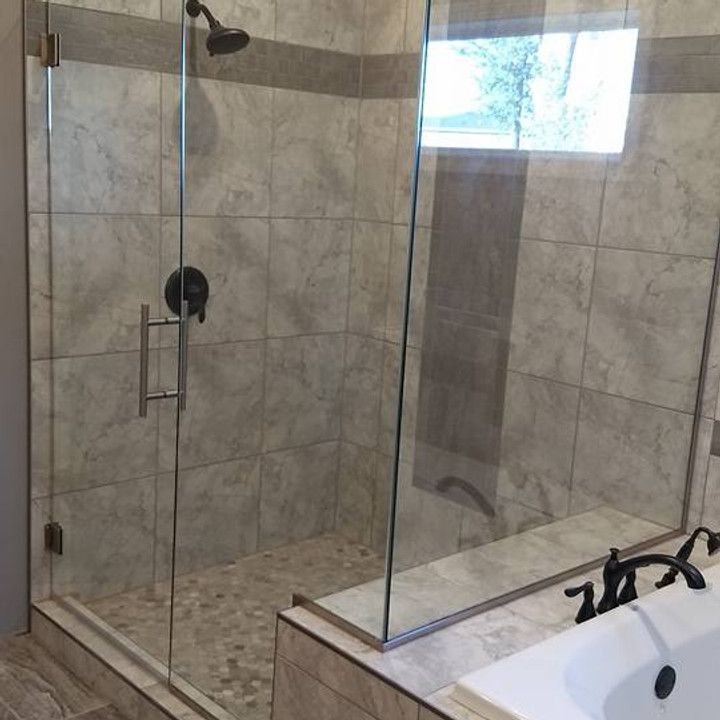 Glass-enclosed shower with gray tiled walls and a pebble floor, black fixtures, and a low curb.