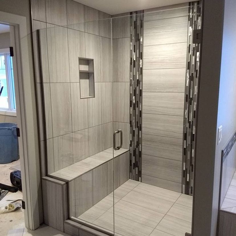 Glass-enclosed shower with gray tiled walls, built-in bench, and decorative tile strip.
