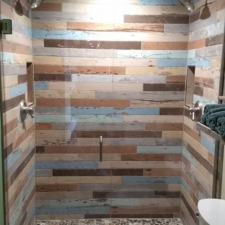 Shower with multicolored wood-look tiles and stone floor. Features two built-in shelves and glass door.
