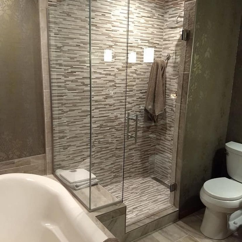 Bathroom with a glass-enclosed shower, stone tile walls, and a white toilet. A towel hangs inside the shower.