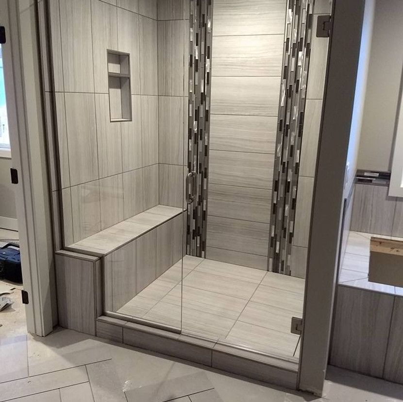 Tiled shower with glass door, built-in bench, and niche; light gray and multi-colored accent tiles.