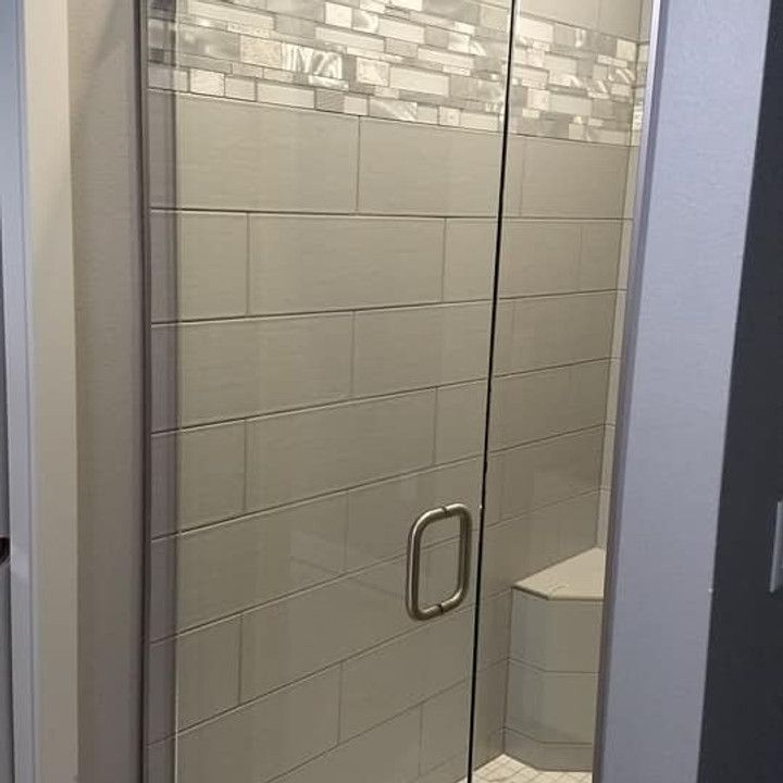 Glass shower door with gray tiled walls and a decorative border.