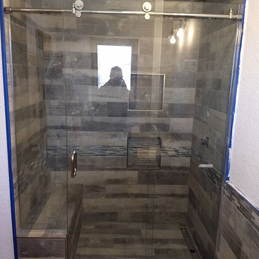 Glass shower enclosure with gray wood-look tile, sliding door, and recessed shelving.