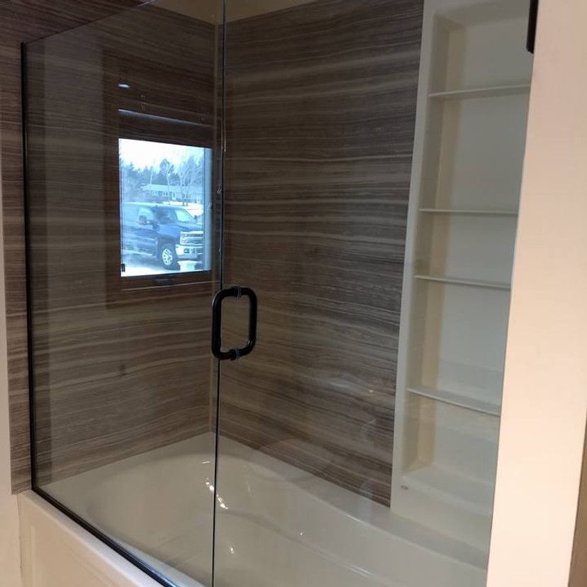 Glass shower enclosure with black hardware, brown tiled walls, white built-in shelves, and a bathtub.