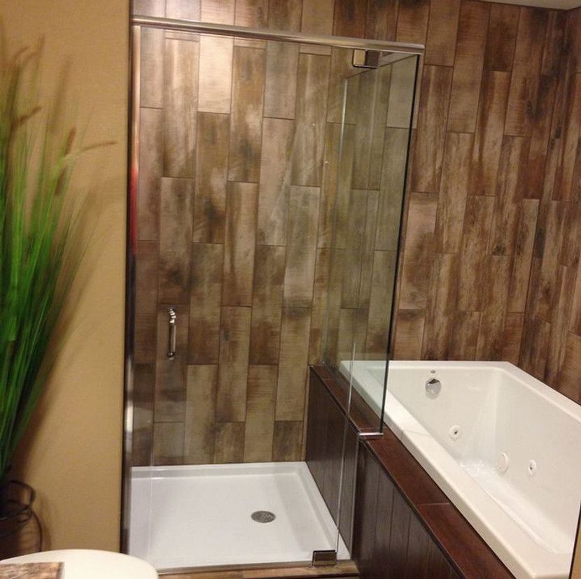 Shower stall and bathtub with wood-look tile. Clear glass shower door and white tub.