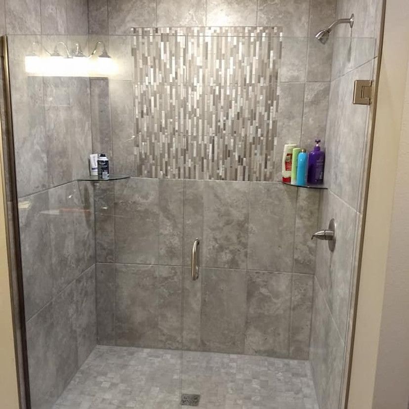 Gray tiled shower with glass door and decorative tile accent. Includes showerhead and product shelves.