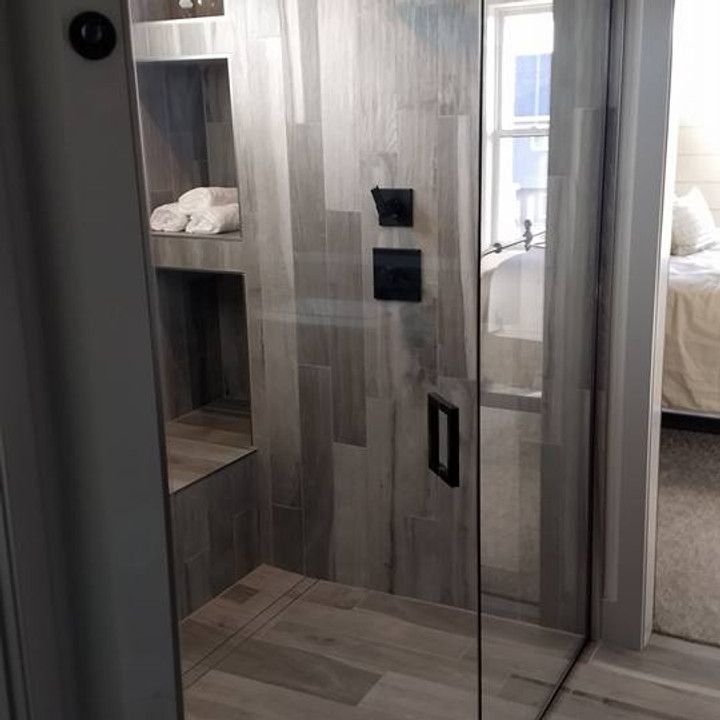 Modern bathroom with a glass shower door and wood-look tile. Towels sit in a built-in shelf.