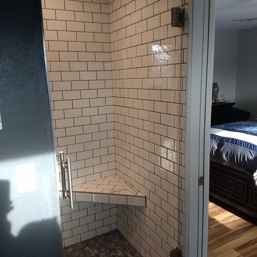 A shower with white subway tile walls, a clear glass door, and a corner seat.