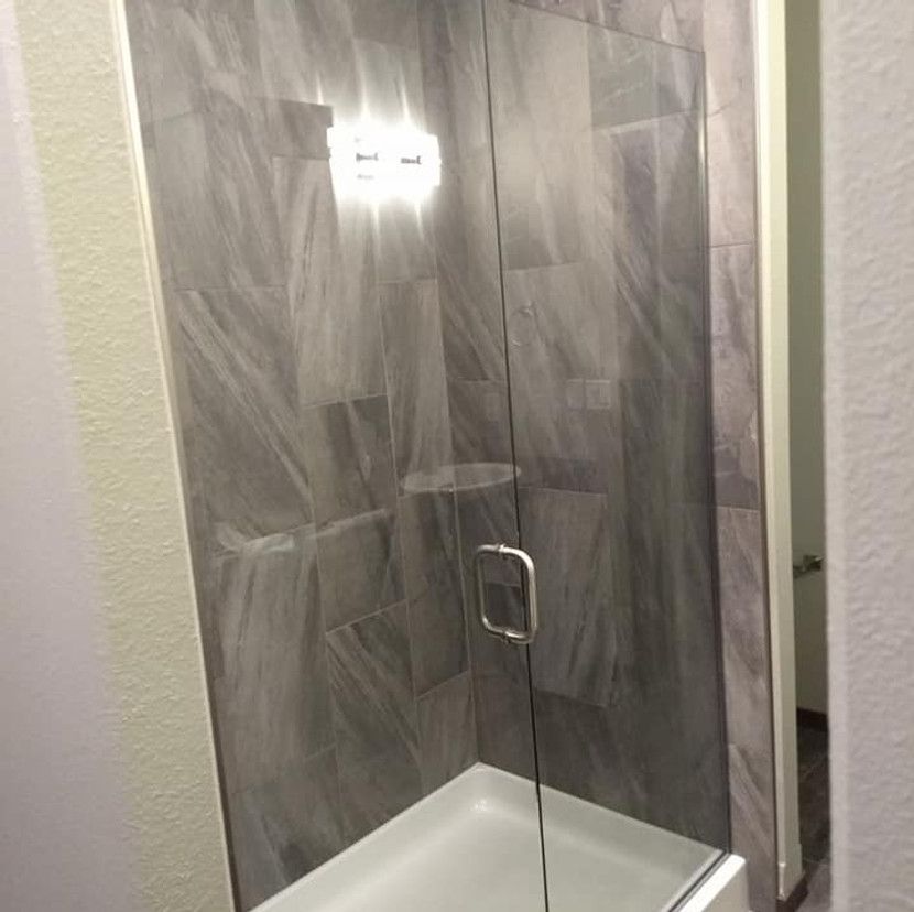 Shower stall with gray tile walls and a glass door. White shower base.
