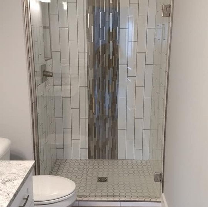 Shower stall with glass doors, white and gray tile walls, and a tiled floor.