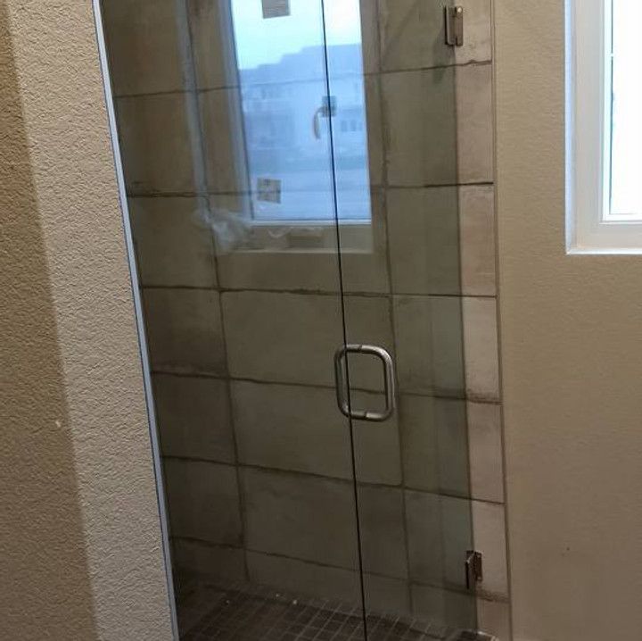 Glass shower door with tiled walls, handle, and hinges.