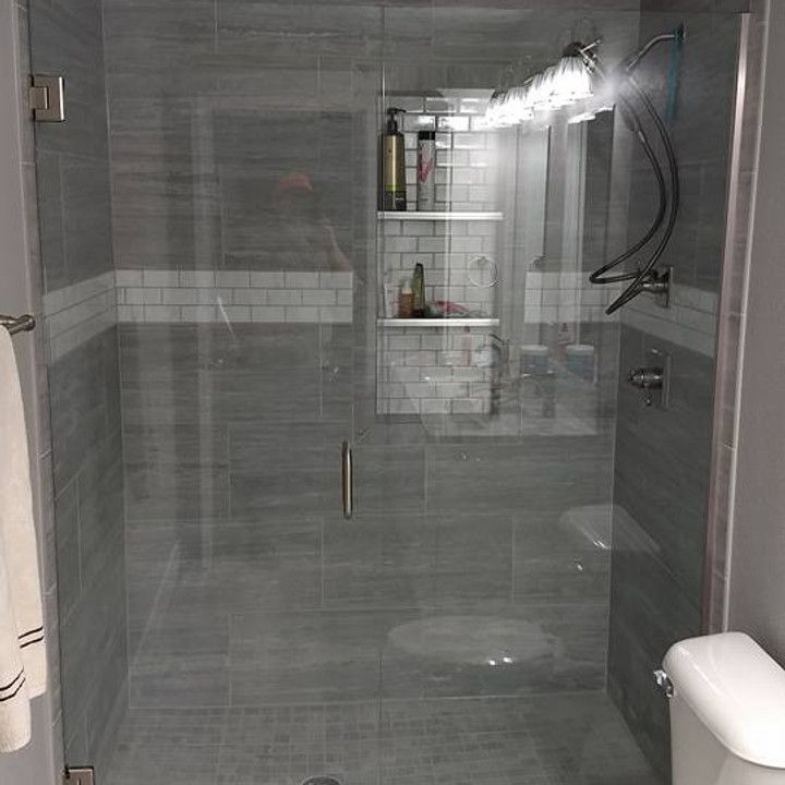 Gray tiled shower with glass doors, built-in shelf, and rain showerhead.
