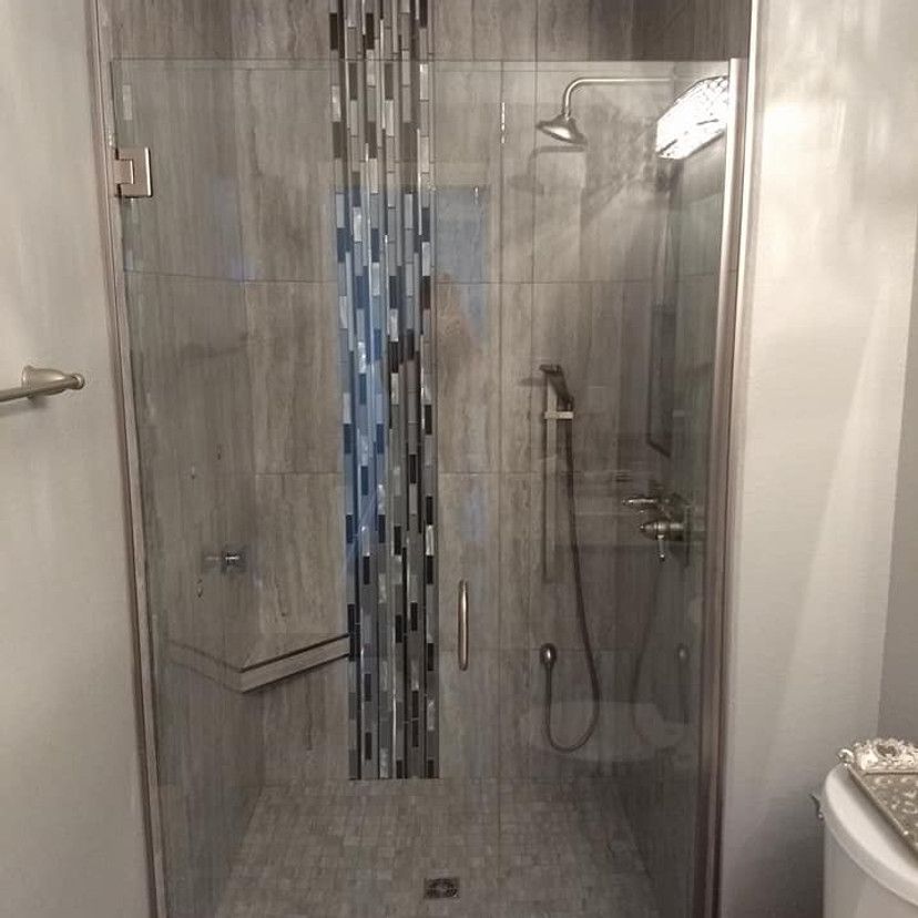 Shower stall with gray tile and a mosaic accent. Glass door and silver fixtures.