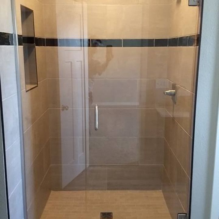 Glass shower enclosure with beige tiled walls, door, and floor. Black tile border.