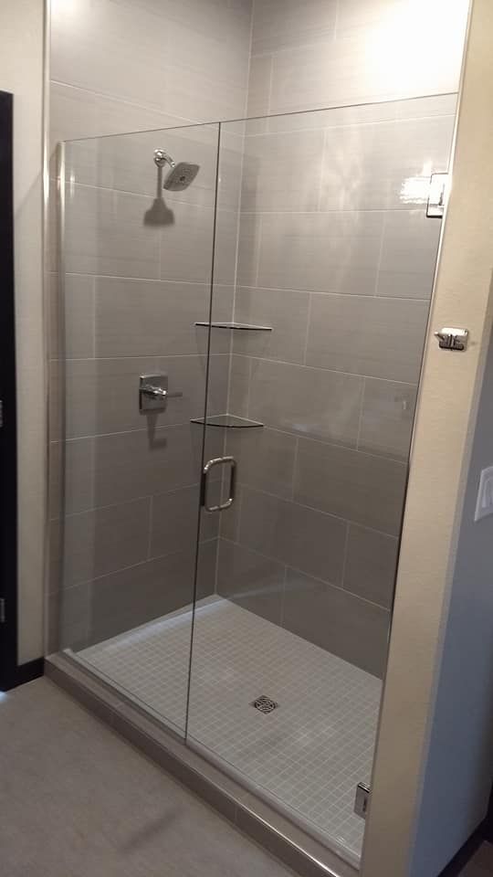 Glass shower enclosure with gray tiled walls and a white shower floor.
