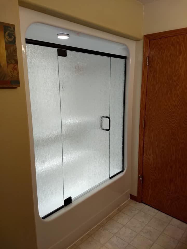 Shower with frosted glass doors, black frame, and a white tub base, next to a closed brown door.