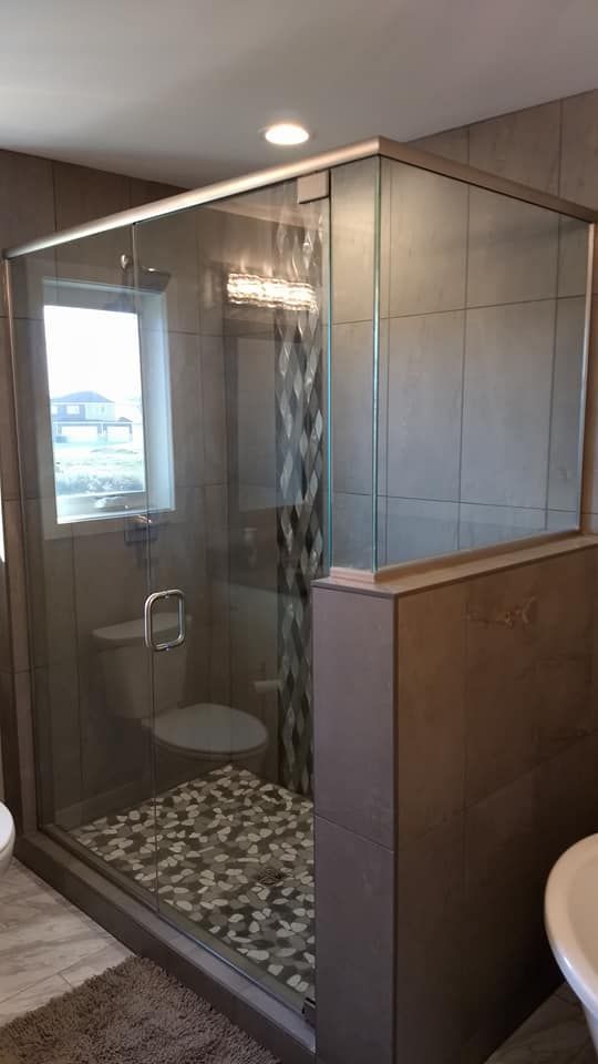 Glass-enclosed shower with pebbled floor and tiled walls. Modern bathroom design with window and decorative lights.
