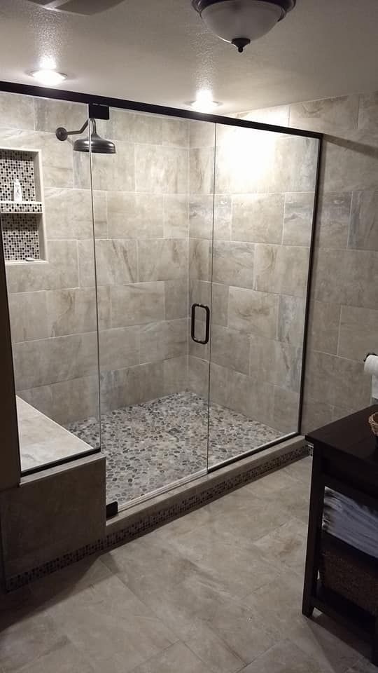 A modern shower with clear glass doors and pebble flooring, surrounded by beige tile.