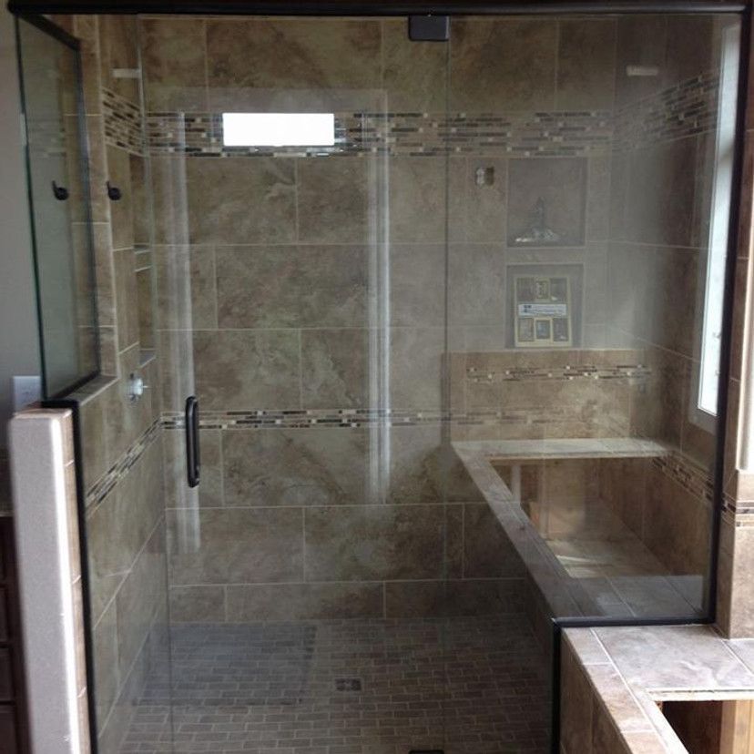 Glass shower enclosure with brown tile walls and a built-in bench.