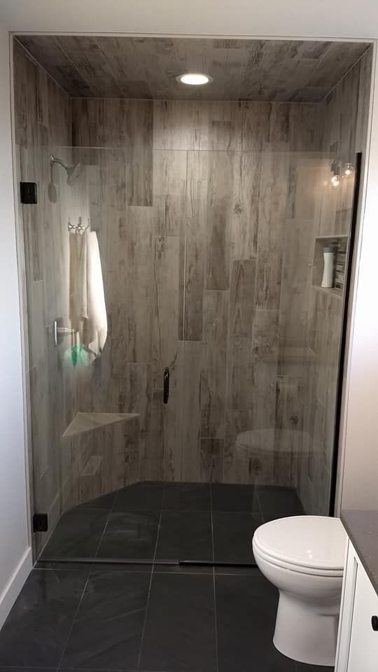 Glass shower with wood-look tile walls, black tile floor, and a white toilet.