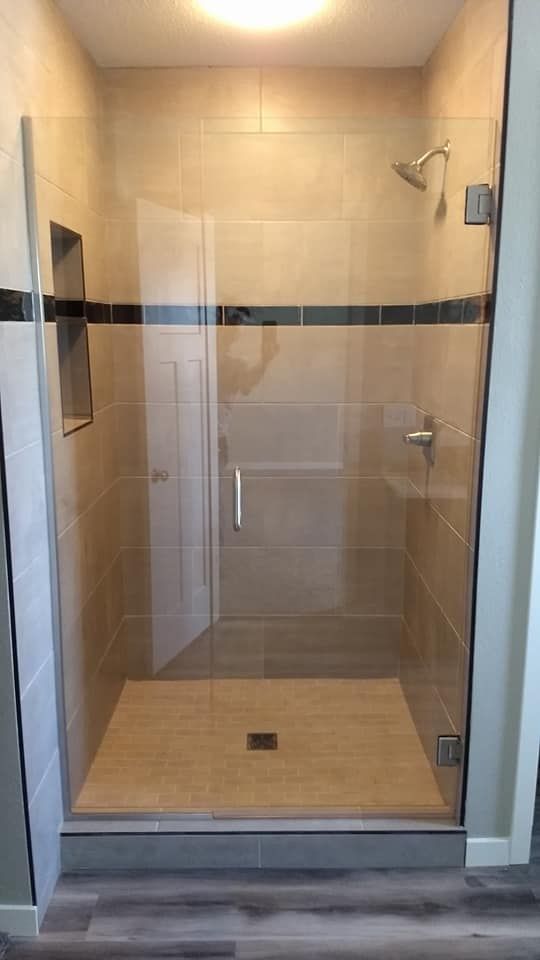 Shower with a glass door, beige tile, chrome fixtures, and a recessed shelf.