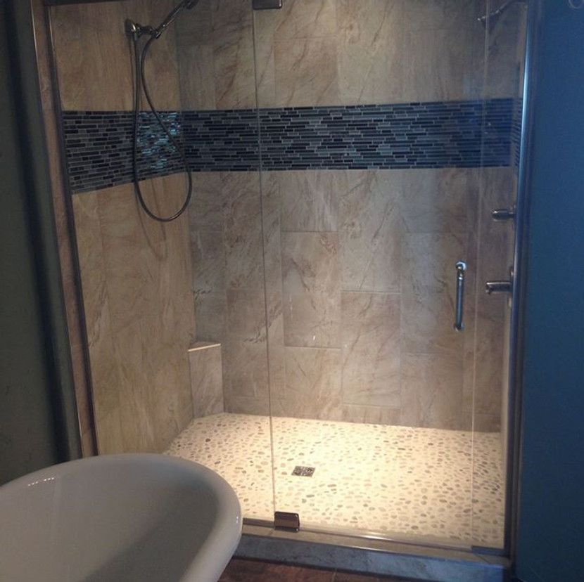 Shower stall with stone tile walls, glass doors, and mosaic tile accent. Tub in the foreground.