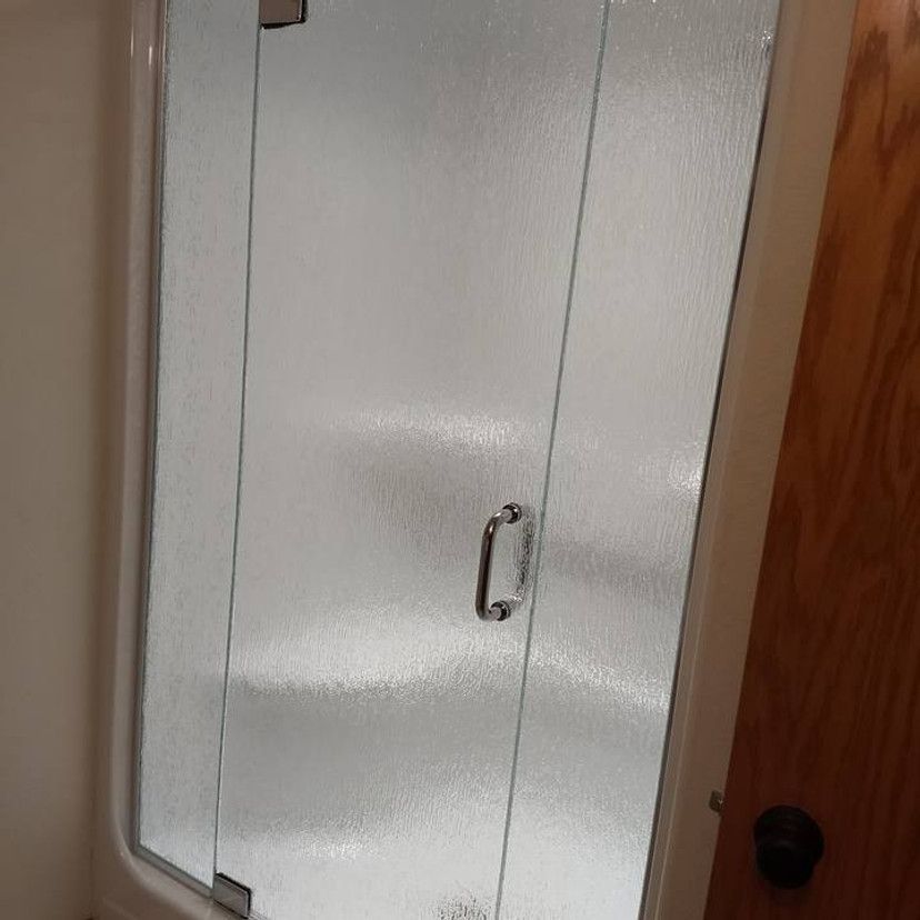 Glass shower door with textured, frosted appearance. Chrome handle and hinges.