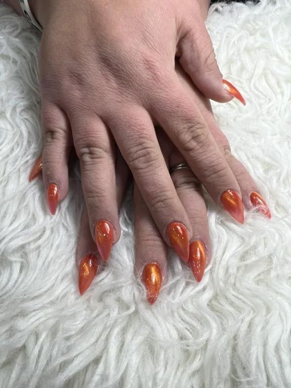 A close up of a person 's hand with long orange nails.