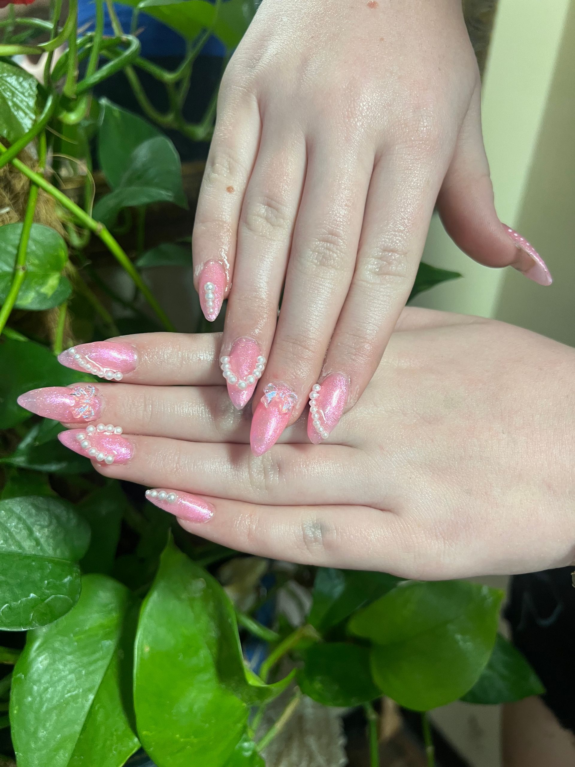 Hands with pink, sparkly, stiletto-shaped nails. Small white beads adorn the tips.