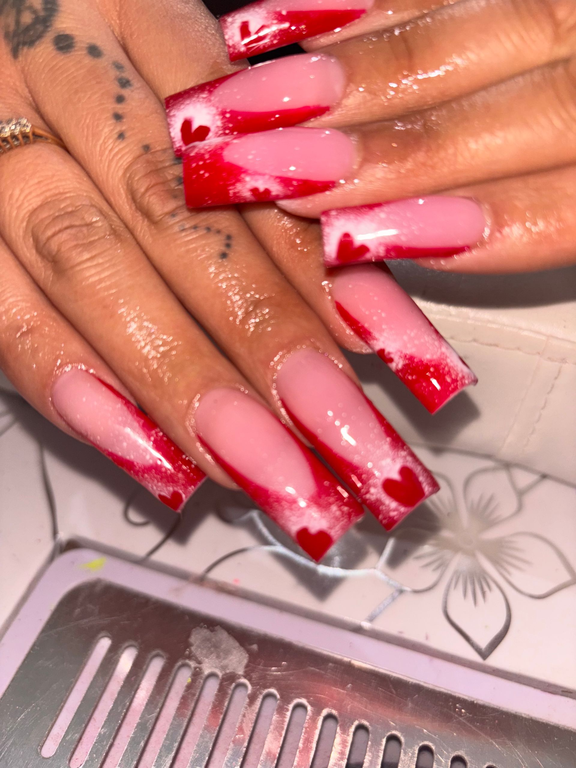 Square acrylic nails with a pink to red ombre design and small heart accents.