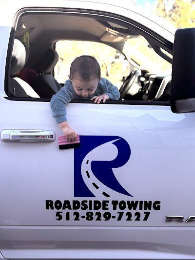 A baby reaching out from a white truck window, wiping the 