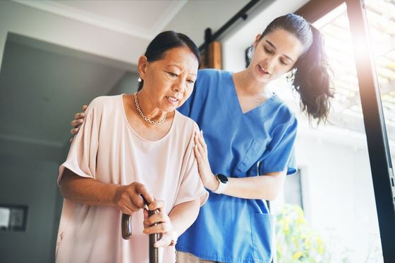 A nurse is helping an elderly woman walk with a cane.