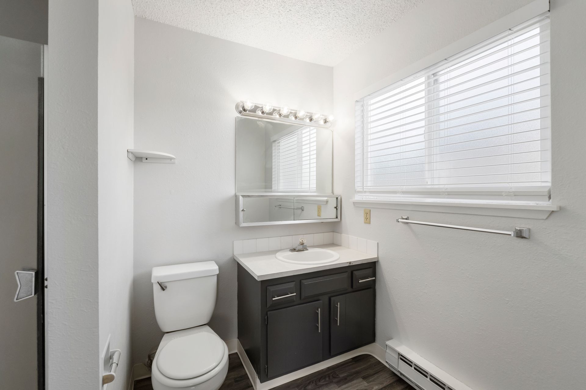 A bathroom with a toilet , sink , mirror and window.