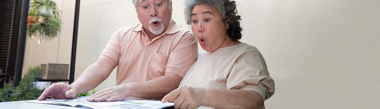 Two senior adults with surprised looks reading a newsletter.