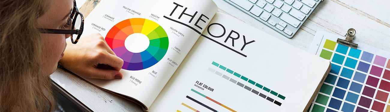 A woman is sitting at a desk reading a book about color theory.