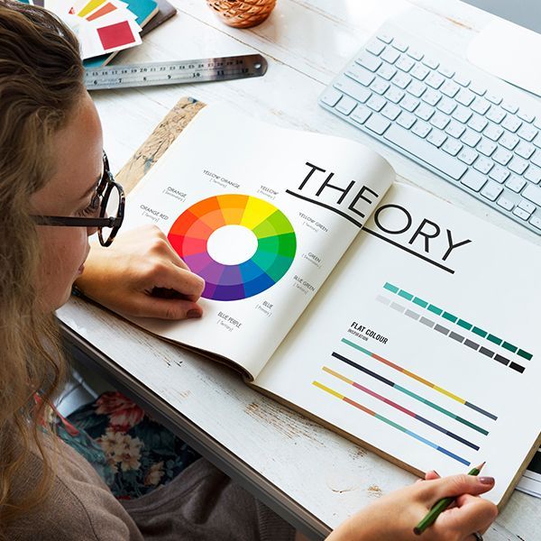 A woman is sitting at a desk reading a book about color theory