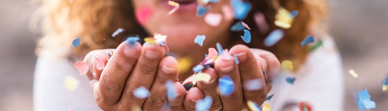 Person blowing colorful confetti from cupped hands.