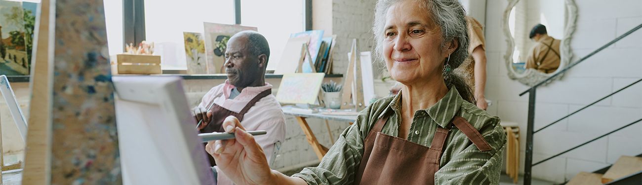 An elderly woman is painting a picture on a canvas in an art studio.