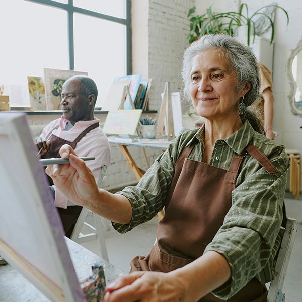 A woman is sitting at an easel painting a picture.
