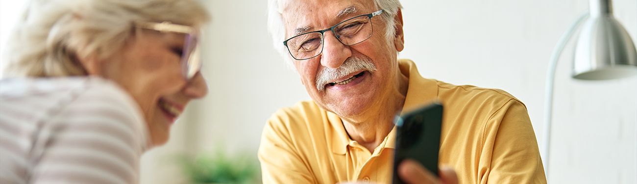An elderly couple is laughing while looking at a cell phone.